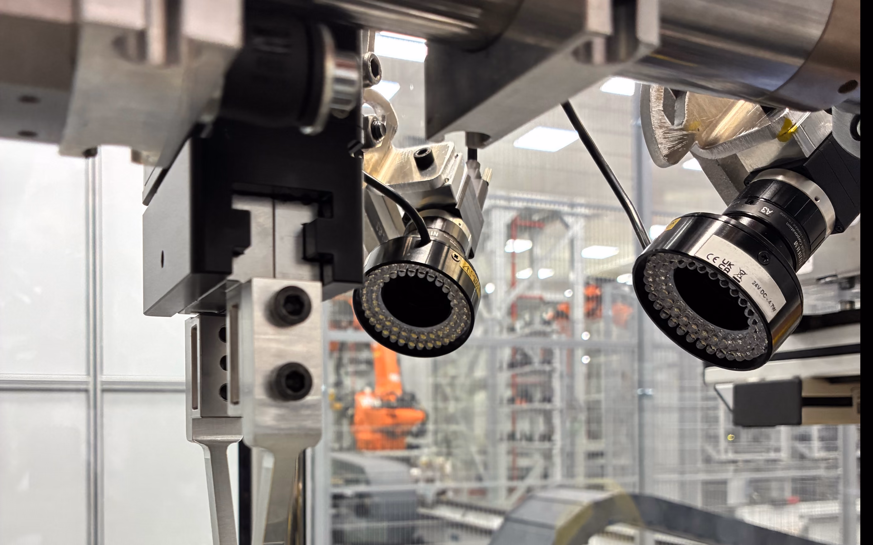 Close-up of a robot wrist carrying a gripper and two ring-lit cameras, on a factory floor